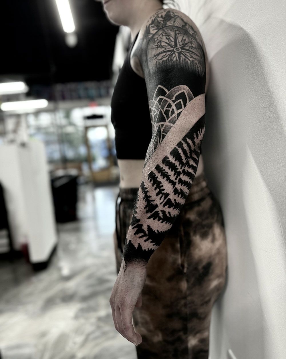 Eine Frau mit einer Tätowierung auf dem Arm lehnt an einer Wand.