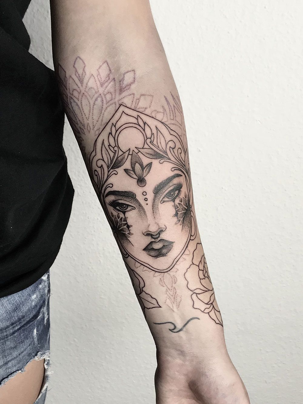 Eine Frau hat auf ihrem Unterarm ein Tattoo mit einem Frauengesicht.