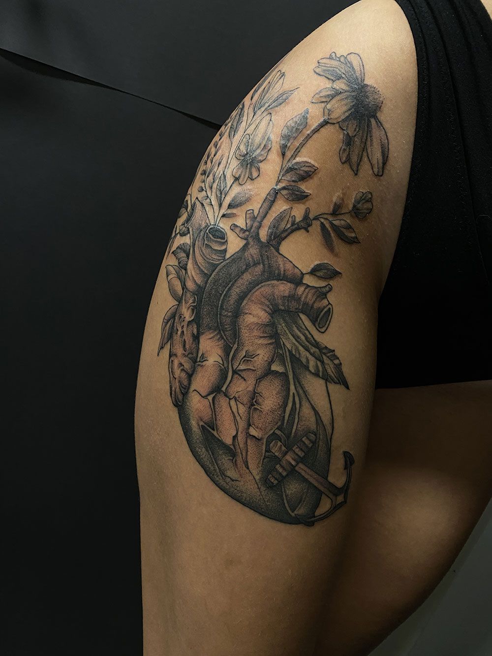 Eine Frau hat ein Tattoo eines Herzens mit Blumen und Blättern auf ihrer Schulter.