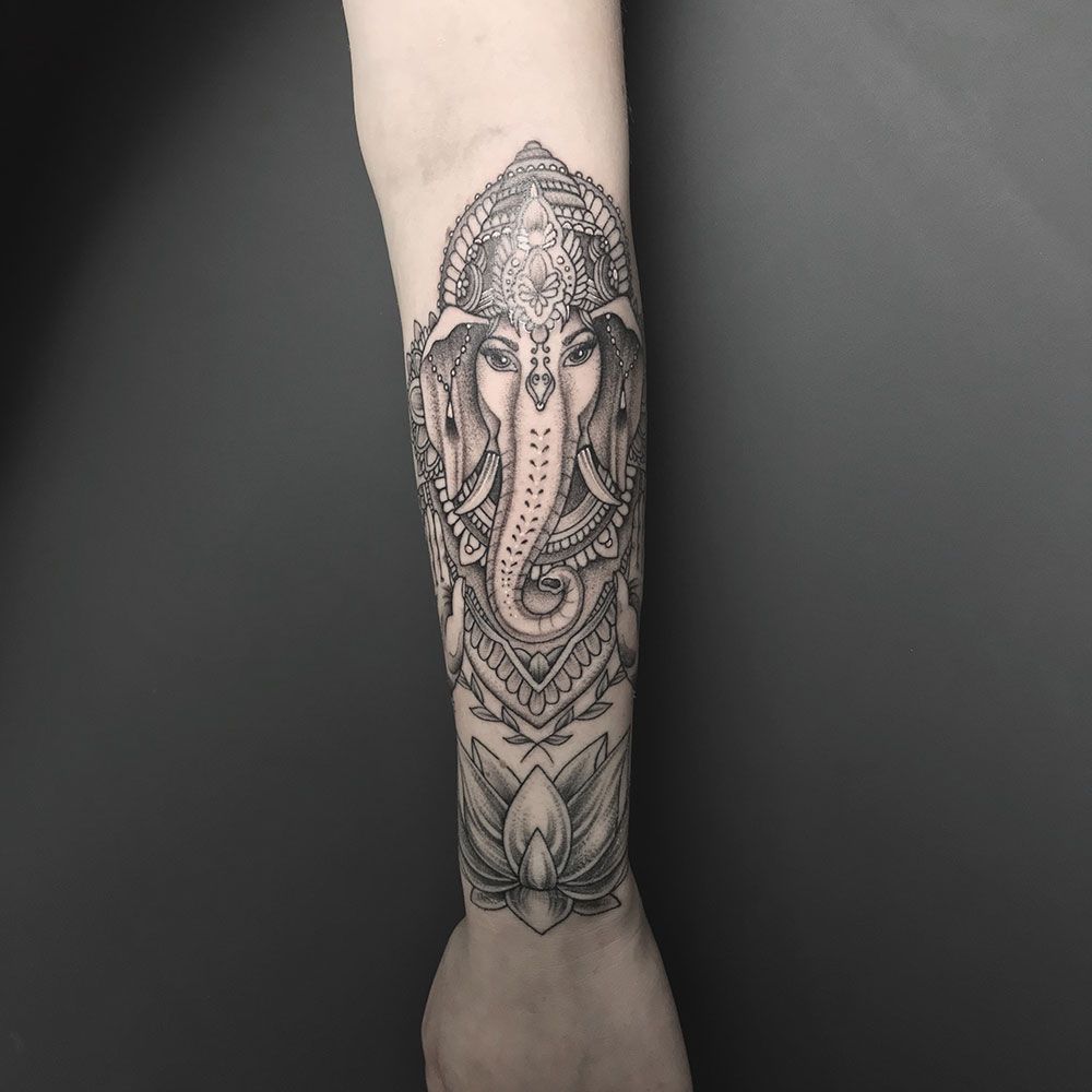 Eine schwarz-weiße Tätowierung eines Elefanten auf dem Unterarm einer Person.
