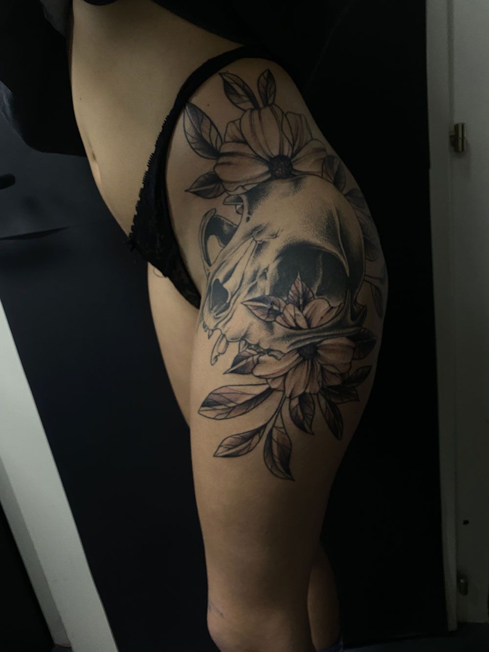 Eine Frau hat ein Tattoo mit einem Totenkopf und Blumen auf ihrem Oberschenkel