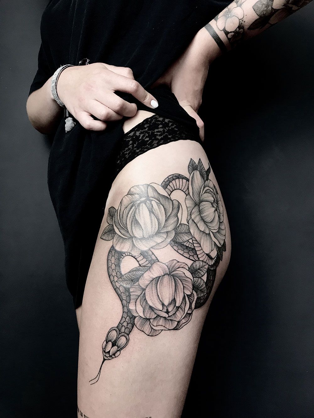 Eine Frau hat eine Tätowierung mit einer Schlange und Blumen auf ihrem Bein.