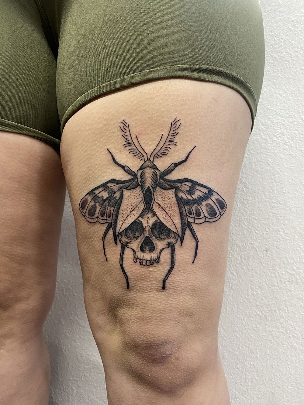 Eine Frau hat eine Motte mit Totenkopf-Tattoo auf ihrem Bein.