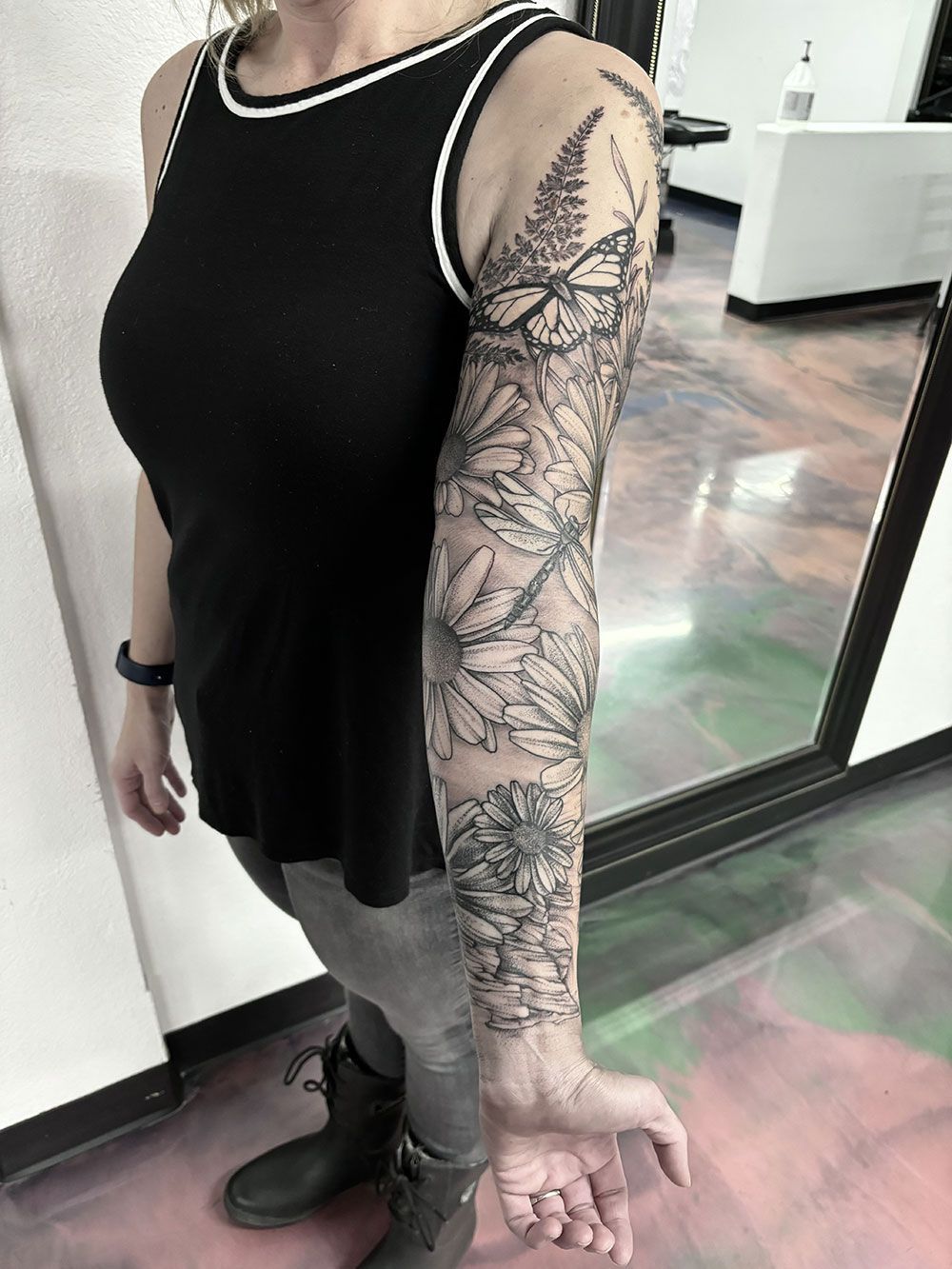 Eine Frau mit einer Tätowierung auf dem Arm steht vor einem Spiegel.