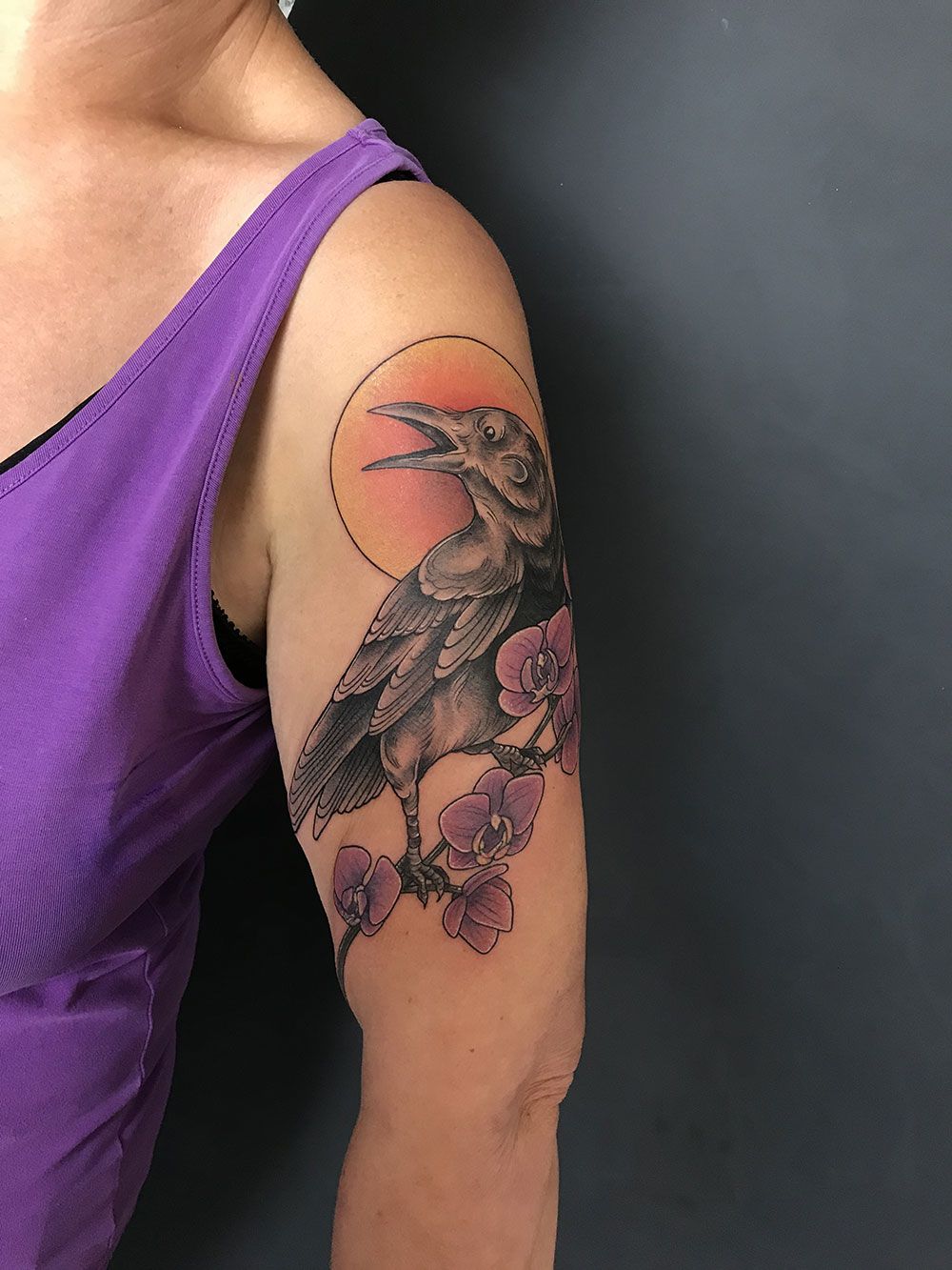 Eine Frau hat eine Tätowierung mit einem Vogel und Blumen auf ihrem Arm.