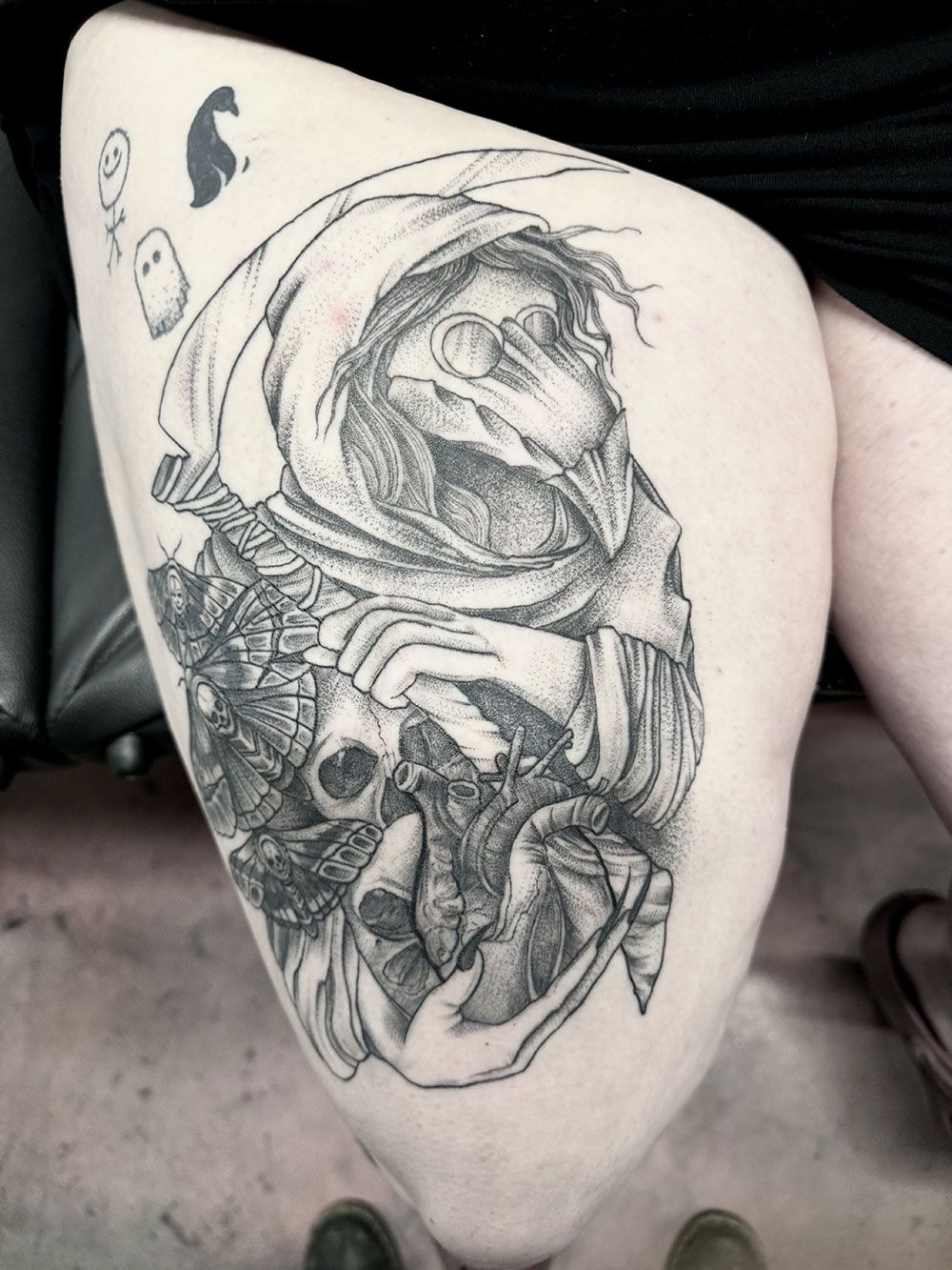 Eine schwarz-weiße Tätowierung eines Pestarztes auf dem Oberschenkel einer Person.