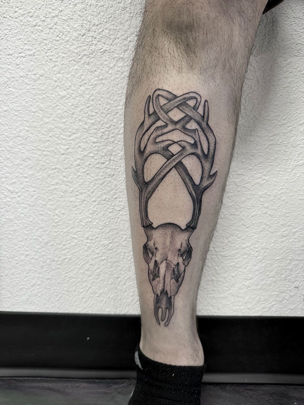 Ein Mann hat eine Tätowierung eines Hirschschädels auf seinem Bein.