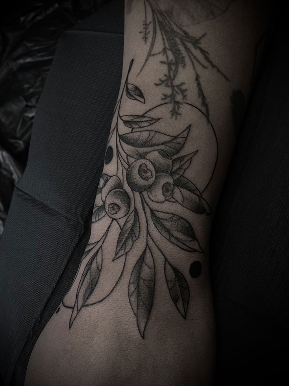Ein schwarz-weißes Tattoo mit Blumen und Blättern auf dem Bein einer Person