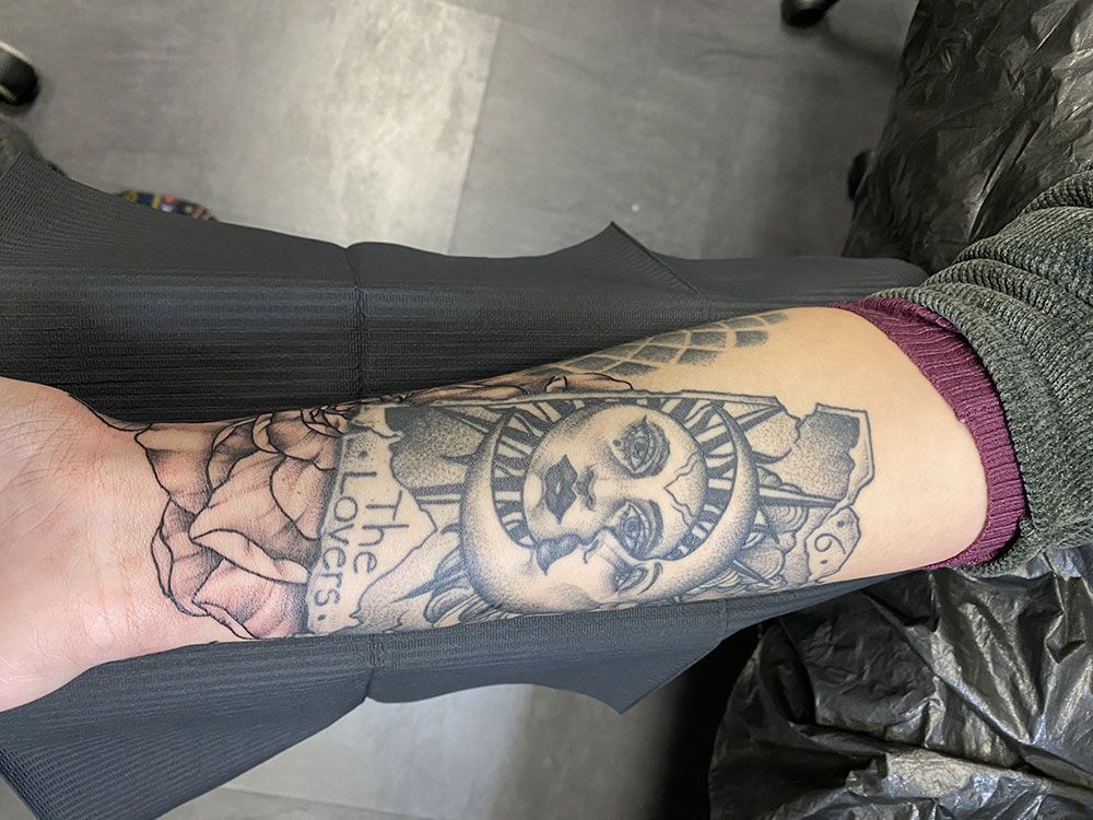 Eine Person mit einer Tätowierung auf dem Arm, auf der „die Liebenden“ steht