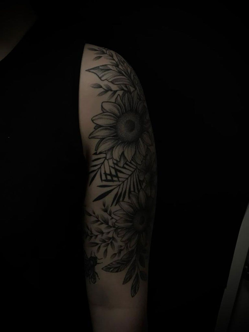 Eine Nahaufnahme des Arms einer Person mit einer Tätowierung aus Blumen und Blättern.