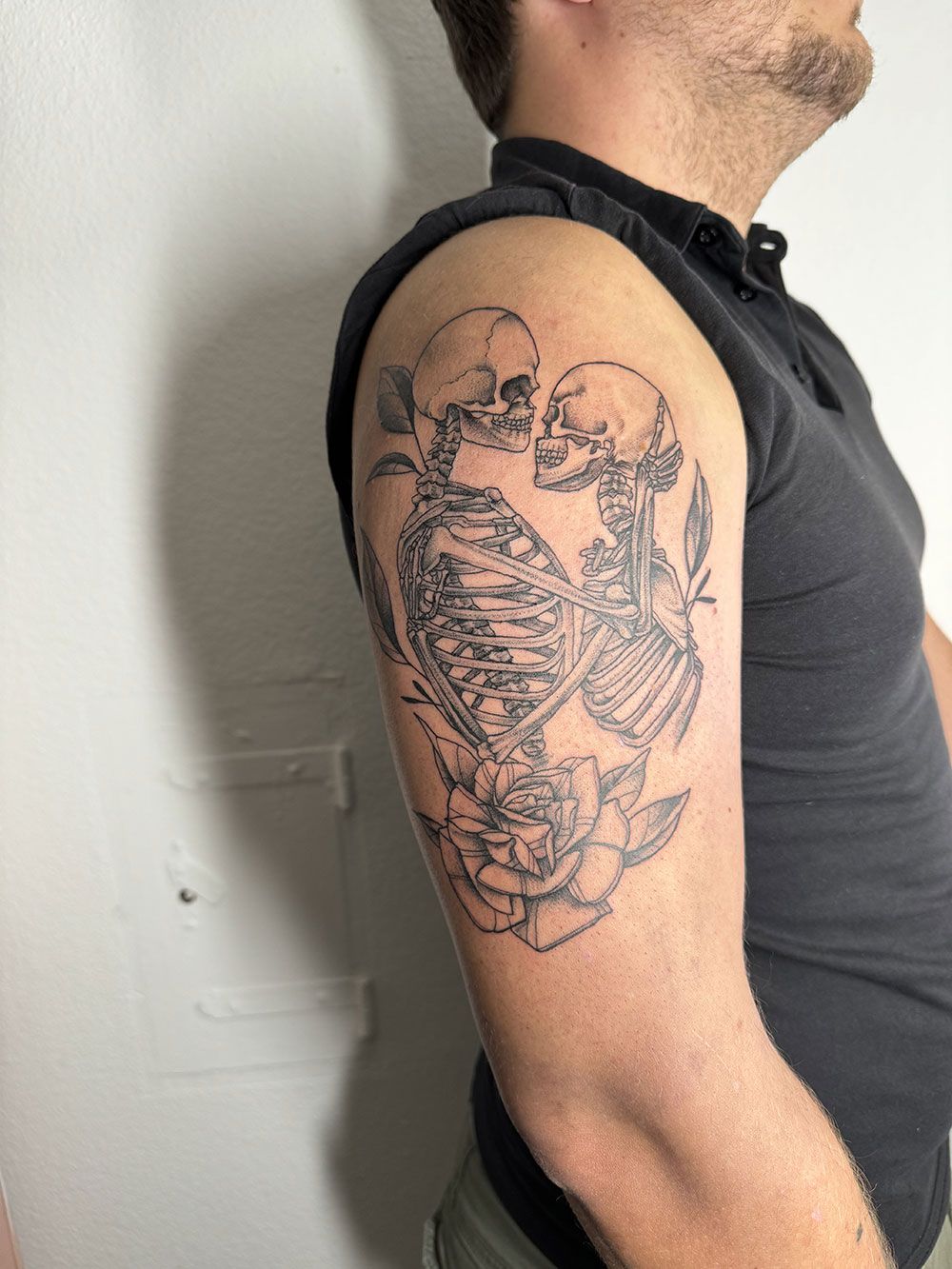 Ein Mann hat auf seinem Arm eine Tätowierung von zwei sich küssenden Skeletten.