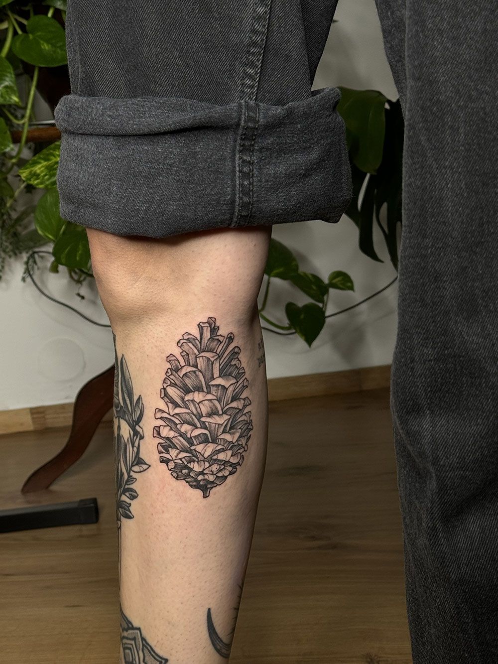 Eine Person mit einem Tannenzapfen-Tattoo auf dem Bein.