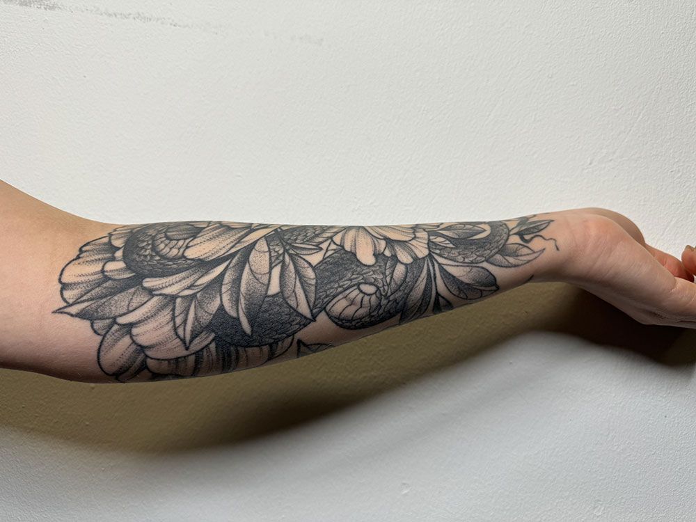 Eine Person hat eine Blumentätowierung auf dem Unterarm.