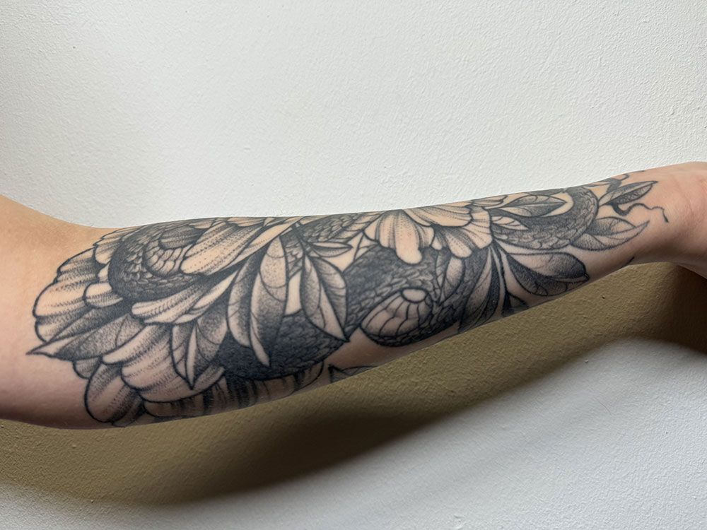 Eine Person hat eine Tätowierung mit Blumen und Blättern auf dem Unterarm.