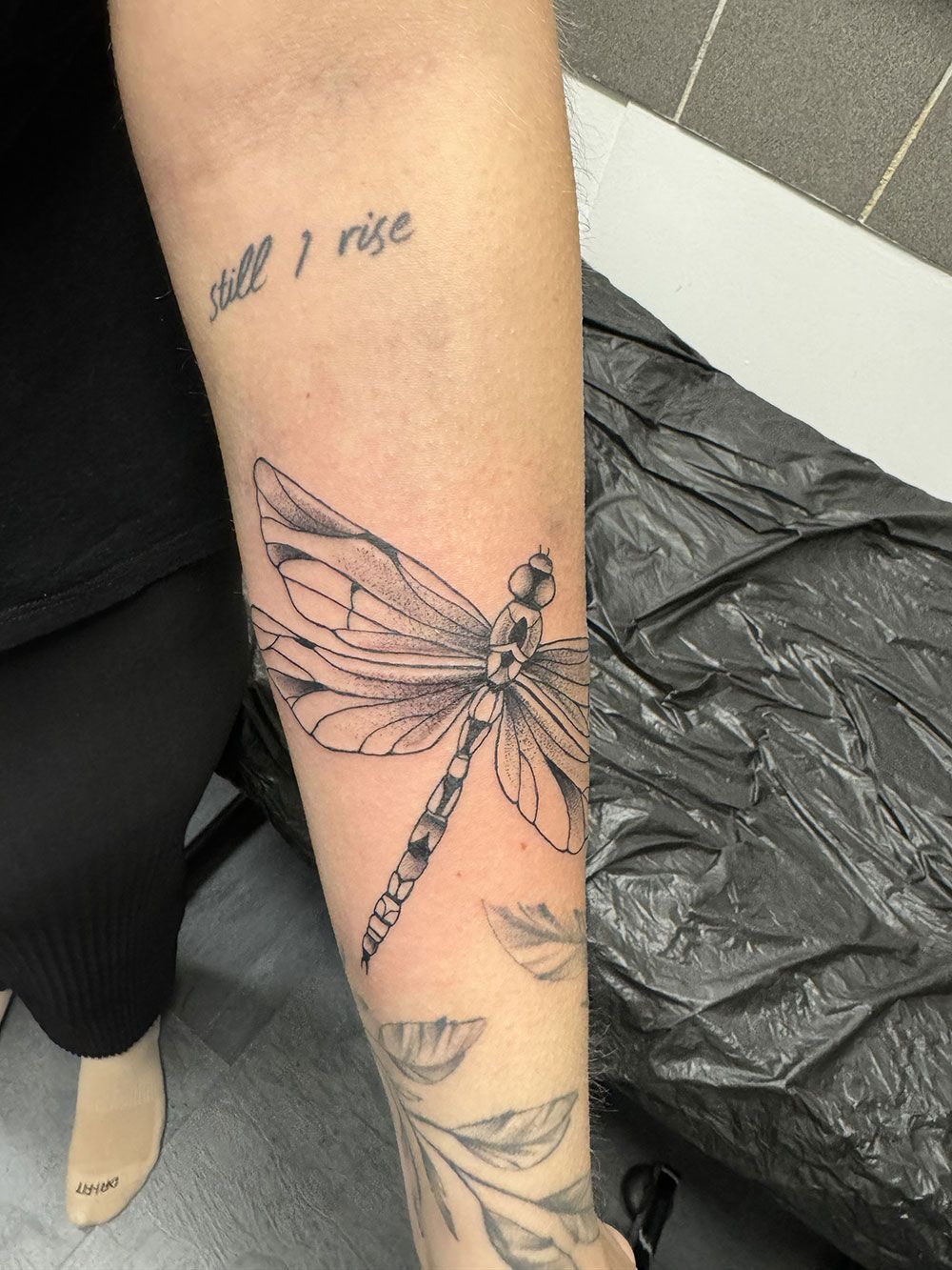 Eine Frau hat eine Libellentätowierung auf ihrem Unterarm.