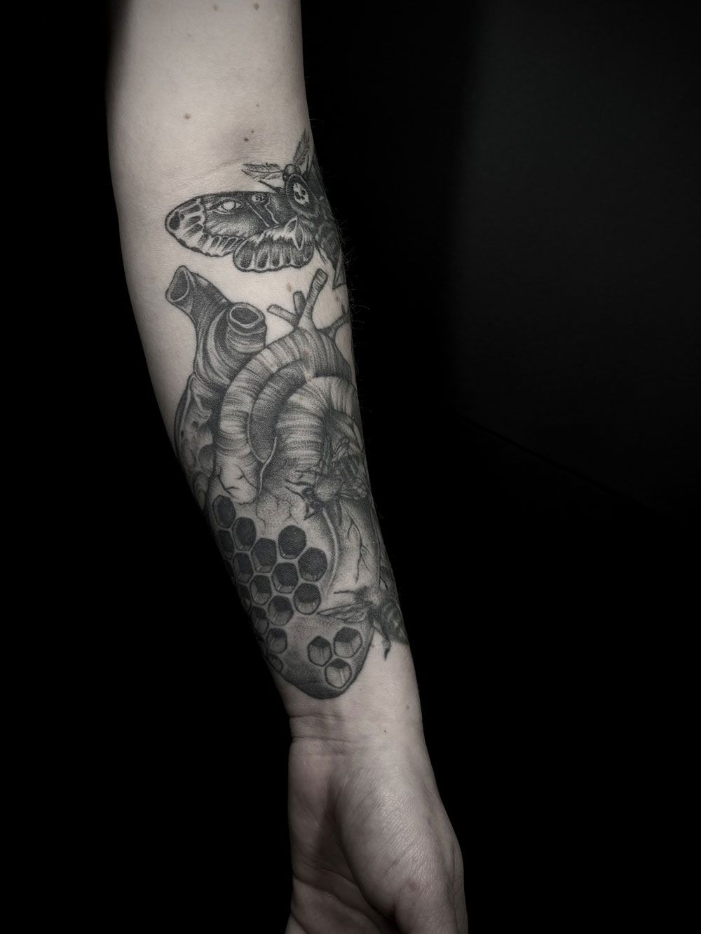 Eine schwarz-weiße Tätowierung eines Herzens auf dem Unterarm einer Person.