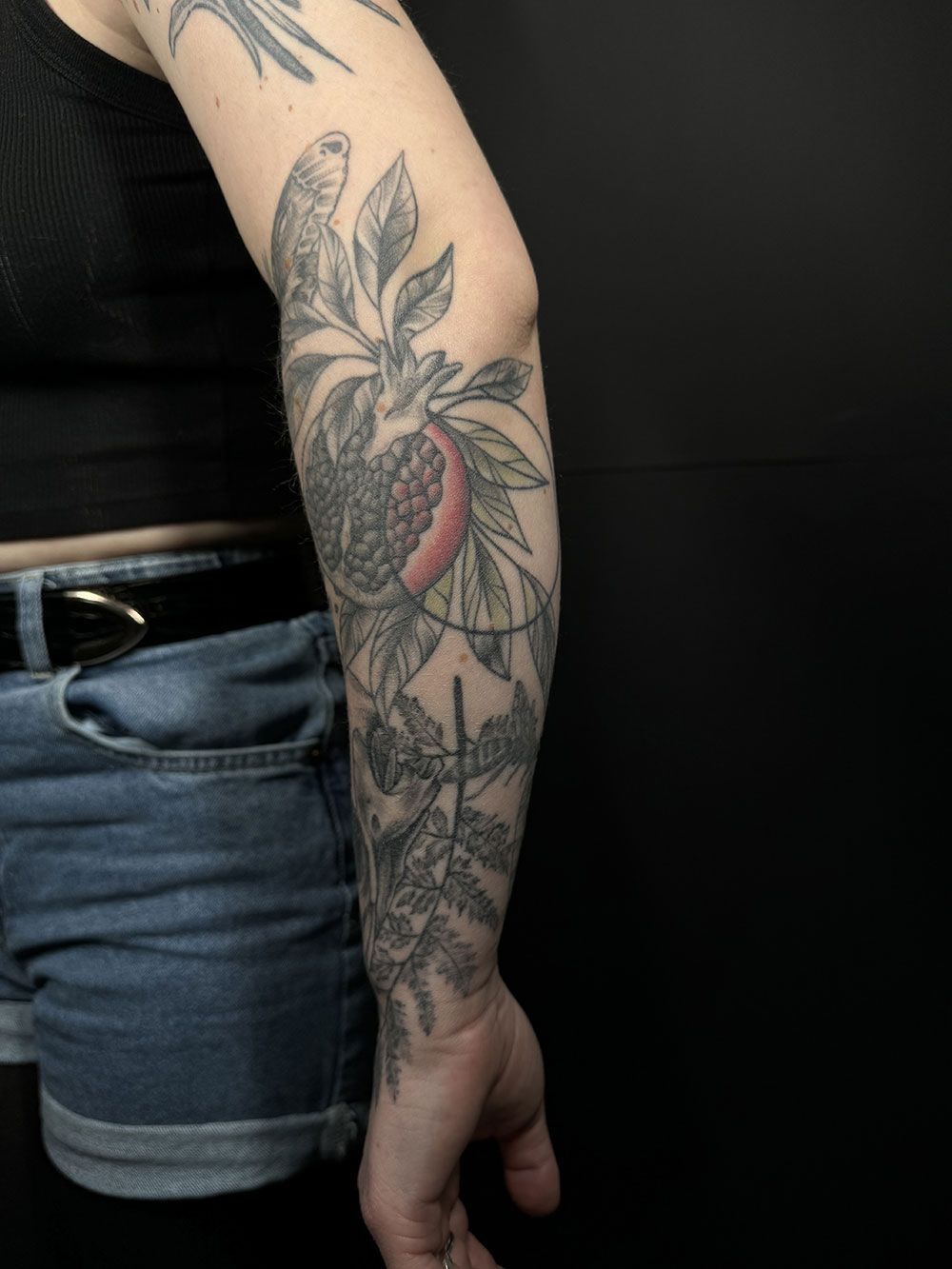 Eine Frau hat eine Tätowierung mit einem Vogel und Blättern auf ihrem Arm.