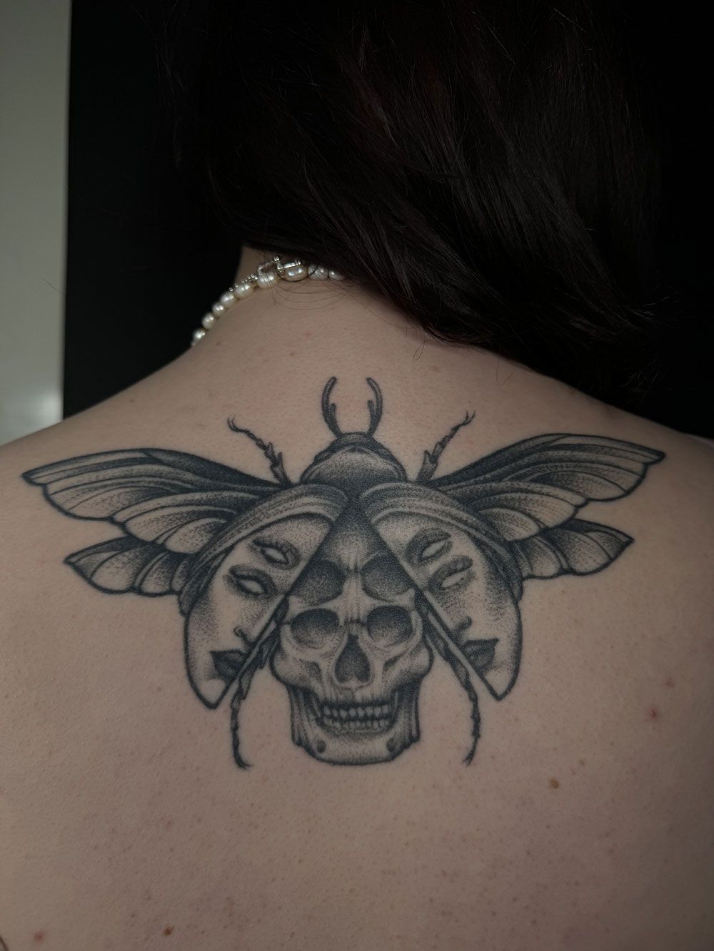 Eine Frau hat ein Tattoo von einem Käfer mit einem Totenkopf auf dem Rücken.