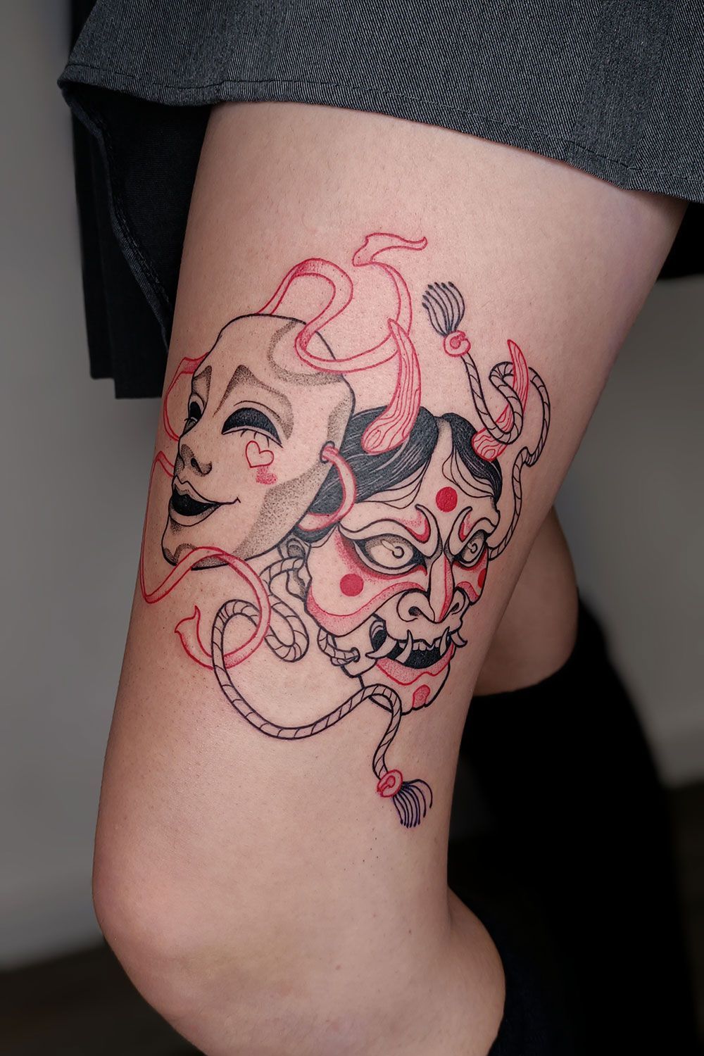 Eine Frau hat eine Tätowierung mit zwei Masken auf ihrem Bein.