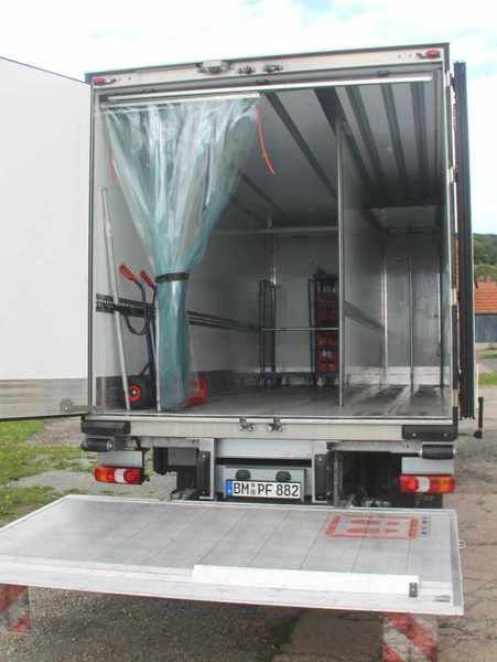 Offene Ladefläche eines Kühlwagens mit Laderampe. Im Inneren befinden sich Regale, ein Vorhang und ein Hubwagen.