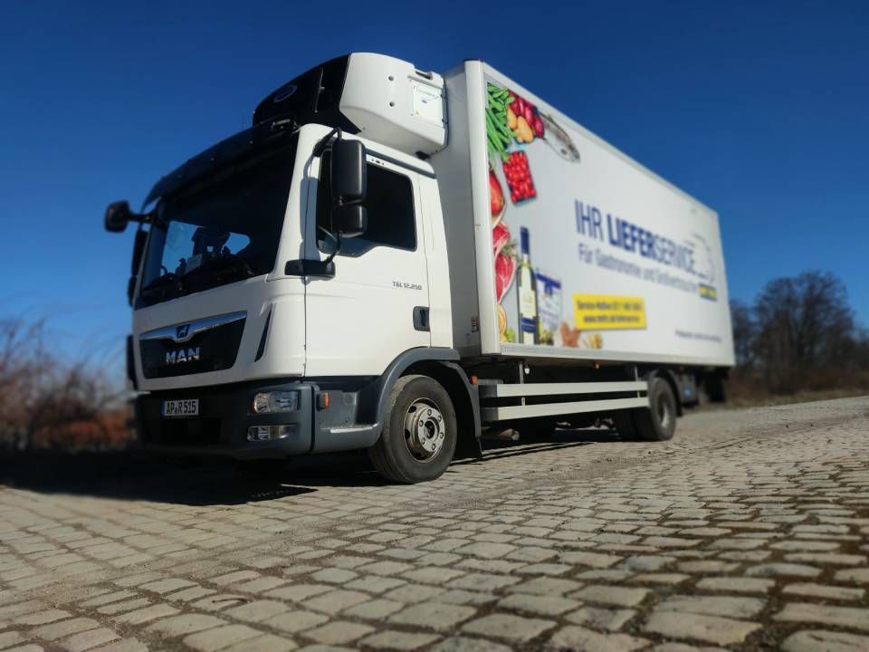 Weißer MAN-Lieferwagen auf Kopfsteinpflaster, Kühlwaren, blauer Himmel im Hintergrund.