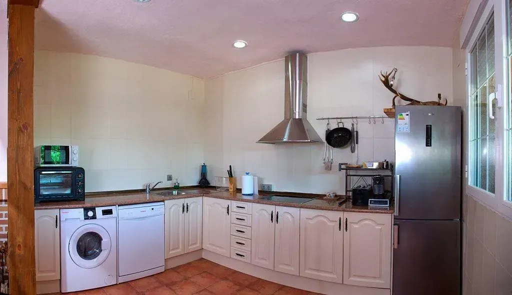 Una cocina con gabinetes blancos, lavadora y secadora, refrigerador y microondas.