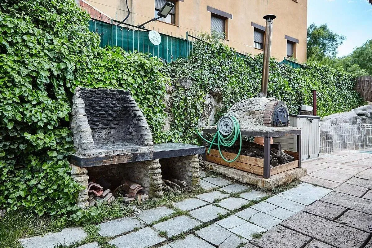 Un banco de piedra está junto a una parrilla de barbacoa en un patio trasero.