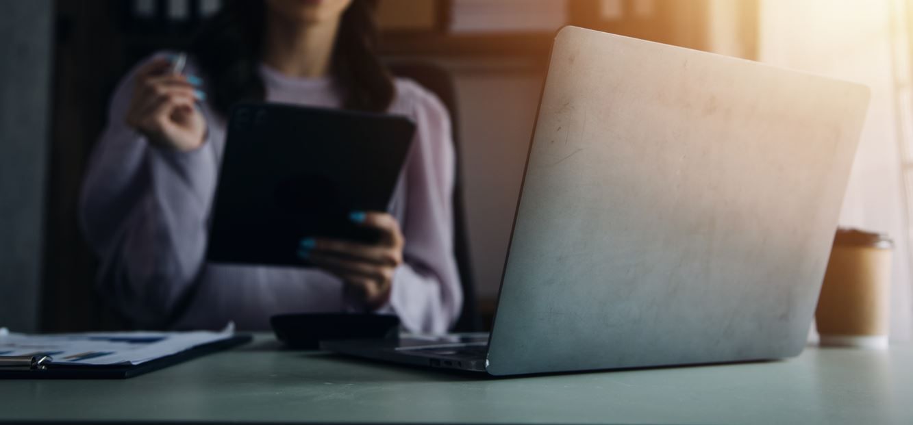 Mujer trabajando con una laptop, con tableta y bolígrafo. Taza de café sobre el escritorio. Luz del sol.