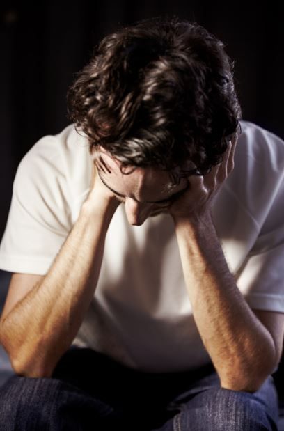 Hombre con la cabeza entre las manos, postura encorvada, en el interior, con aspecto angustiado.