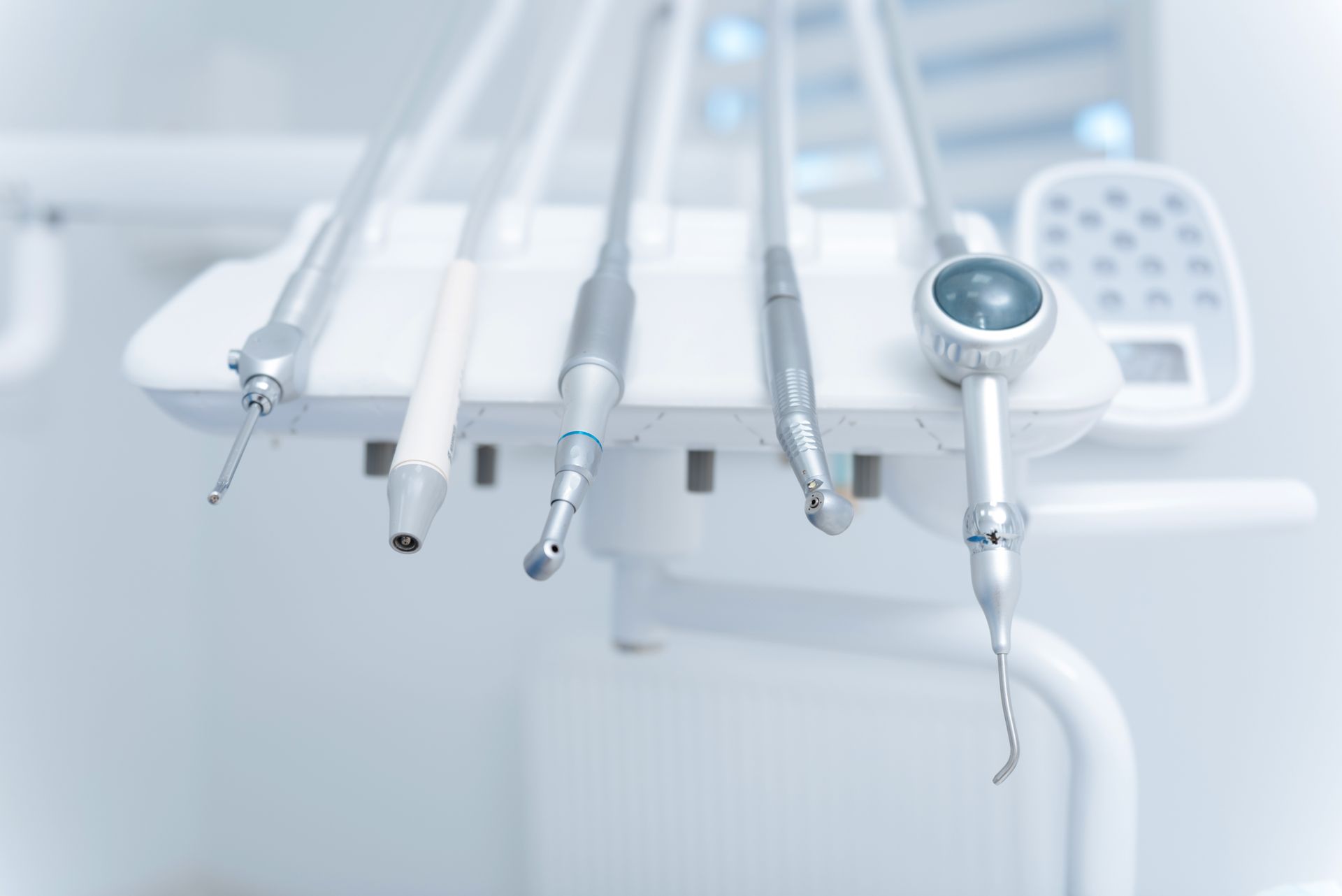 Des instruments dentaires sont accrochés à un fauteuil de dentiste blanc, avec un petit écran en arrière-plan.