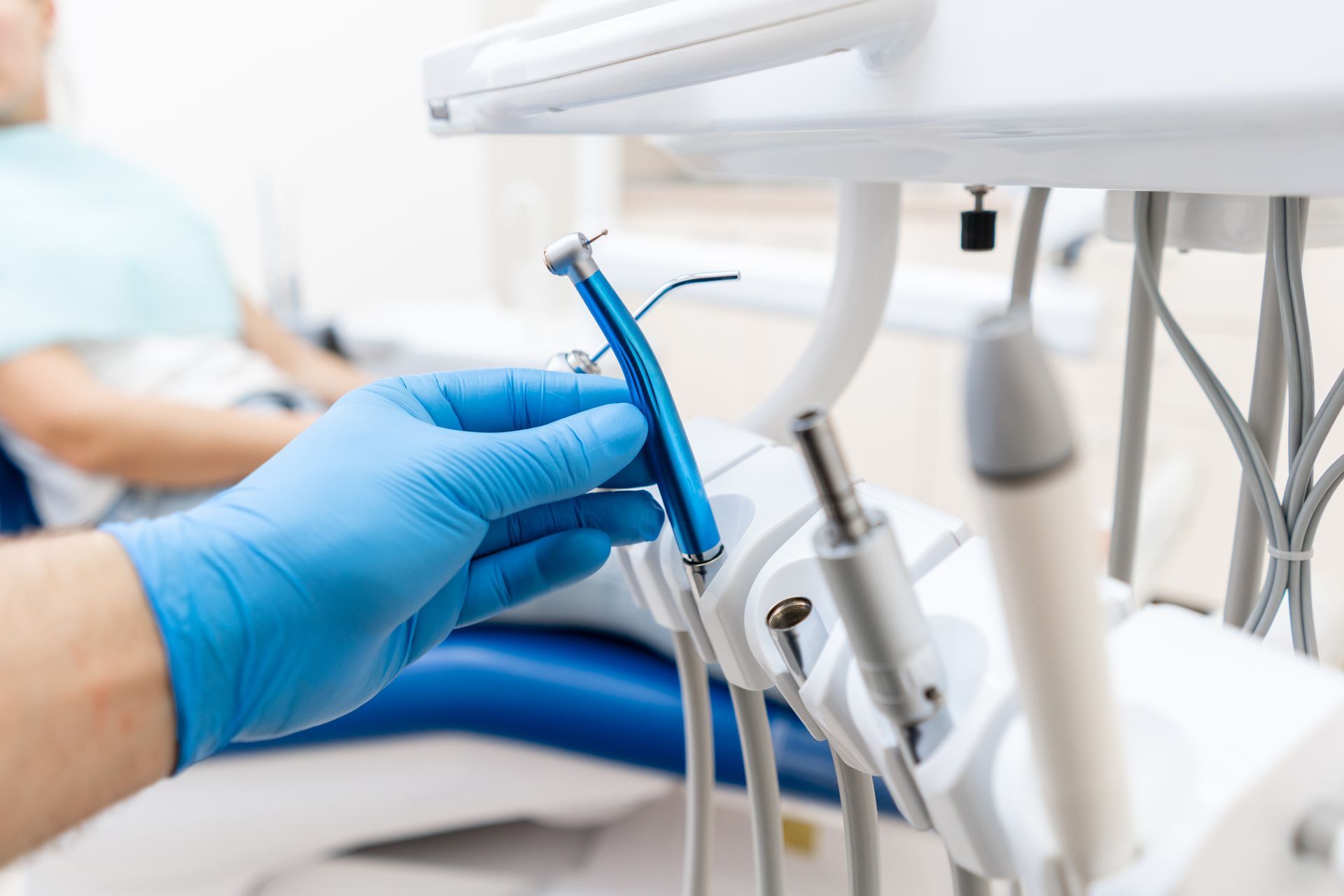 Des mains gantées ajustent un instrument dentaire bleu sur un fauteuil de clinique.