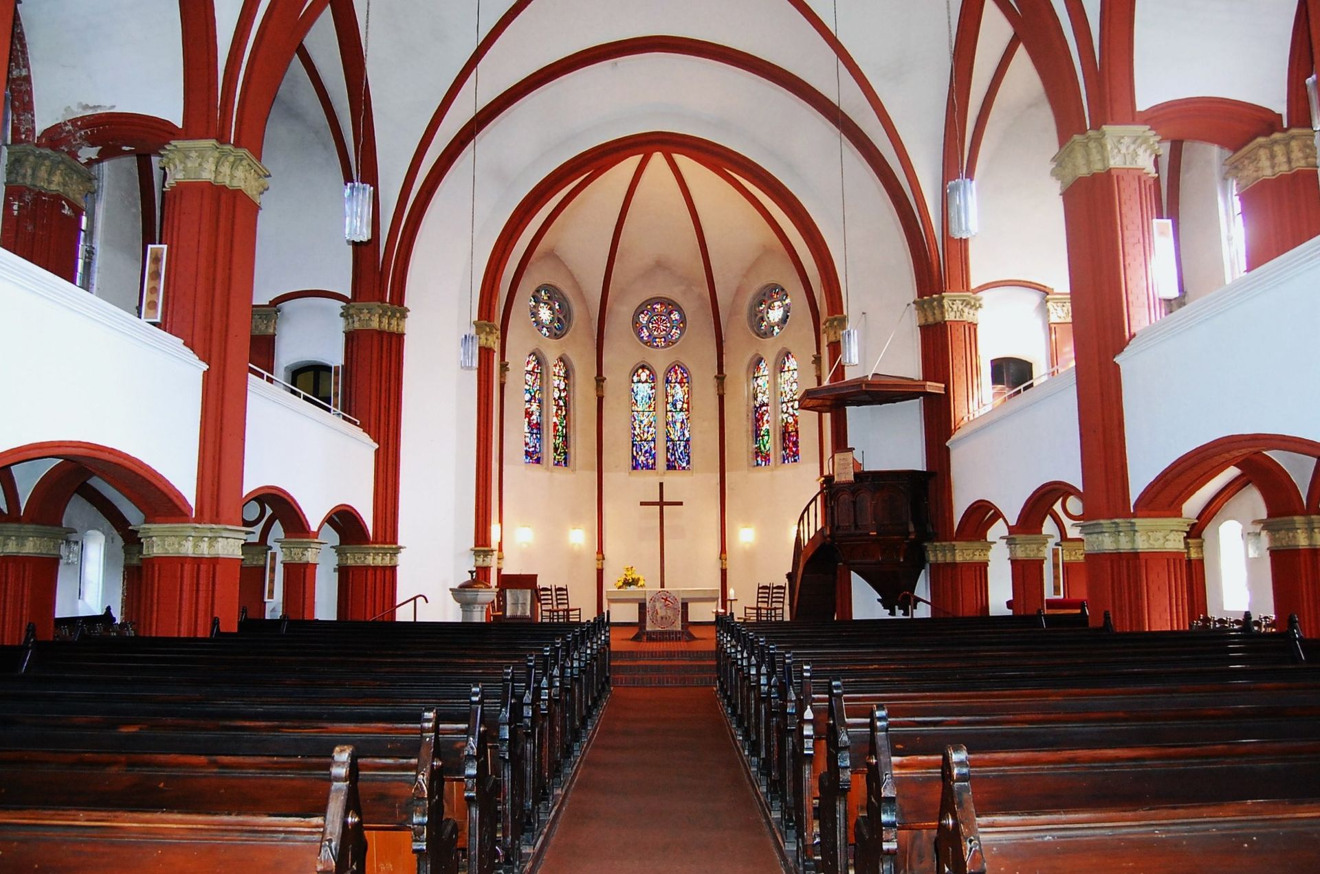 Der Innenraum einer Kirche. Zu sehen sind unter anderem unte Fenster und ein Kreuz im Chorraum.