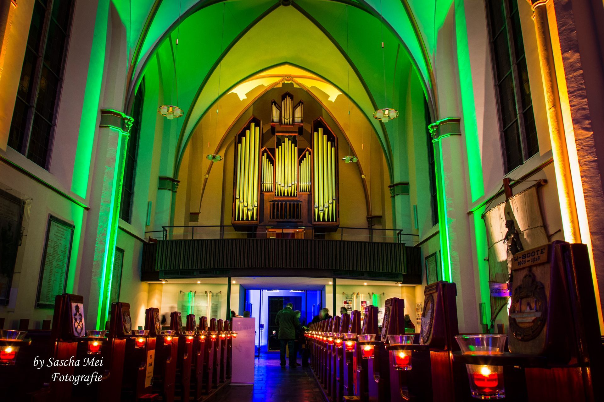 Der Innenraum einer Kirche. Zu sehen sind u.a. hellgraue Bankreihen, eine geschnitzte Kanzel und ein Altar mit Retabel.