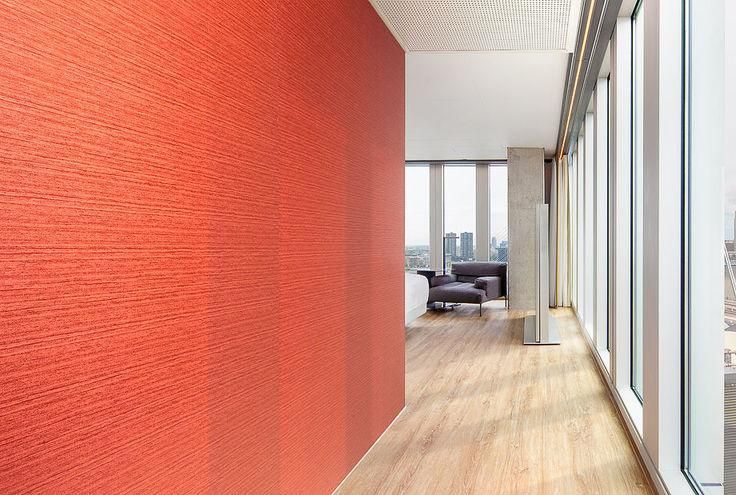 Un pasillo con una pared roja y muchas ventanas que conducen a una sala de estar.