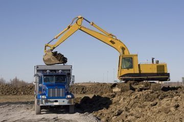 Una excavadora amarilla está cargando tierra en un camión volquete.