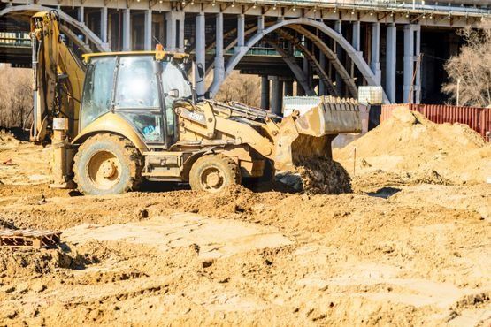 Una excavadora está moviendo tierra en un sitio de construcción debajo de un puente.