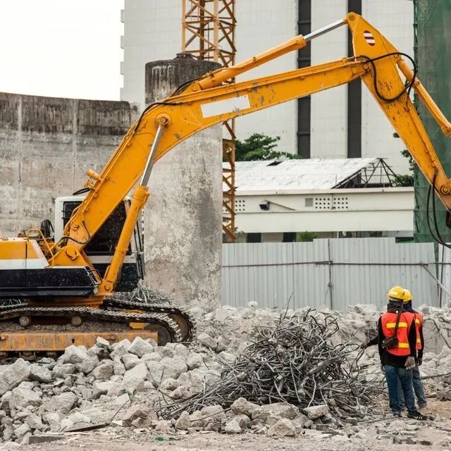 Dos trabajadores de la construcción están parados frente a una gran excavadora amarilla.