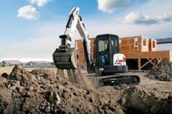 Una pequeña excavadora está cavando un hoyo en la tierra frente a una casa en construcción.