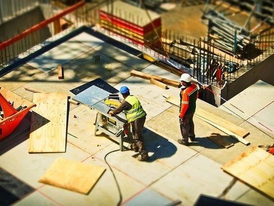 Dos trabajadores de la construcción están cortando madera en una sierra de mesa en un sitio de construcción.
