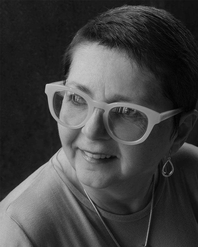 Mujer con gafas sonríe, mirando a la derecha. Retrato en blanco y negro.