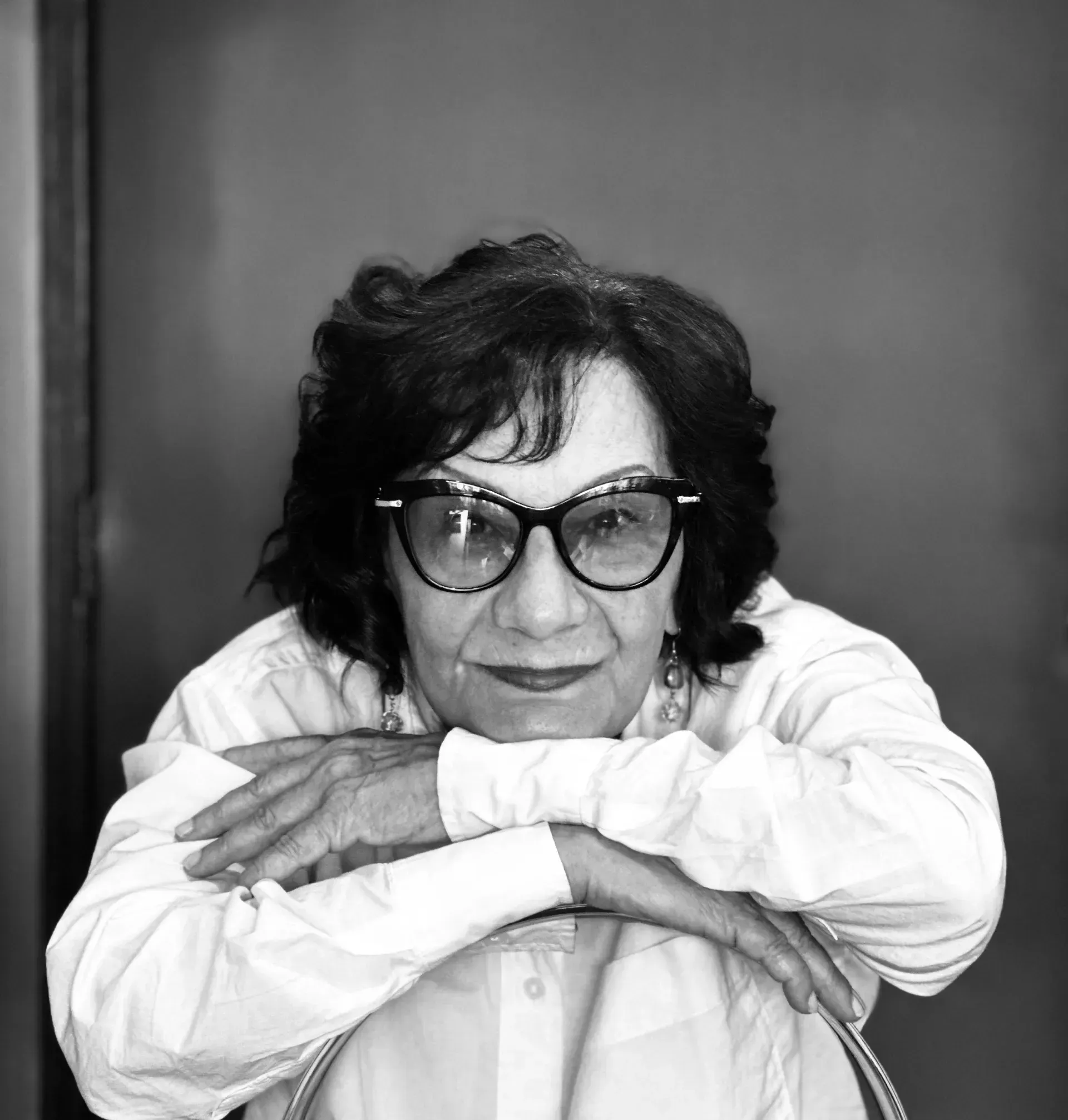 Mujer con gafas, brazos cruzados, apoyada en una silla. Retrato en blanco y negro.