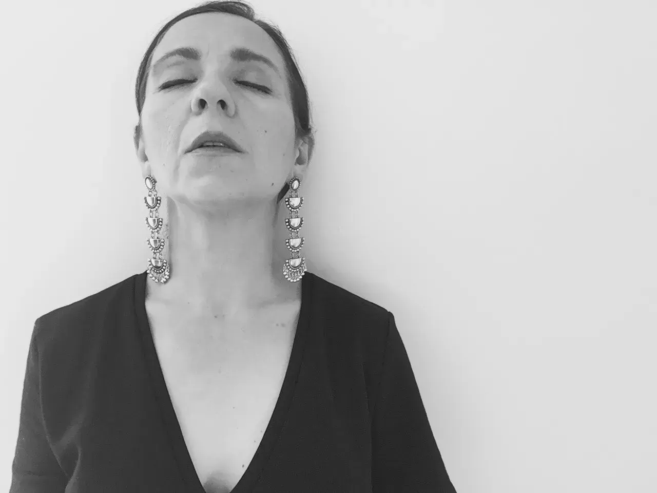 Mujer con los ojos cerrados y pendientes colgantes, en blanco y negro.