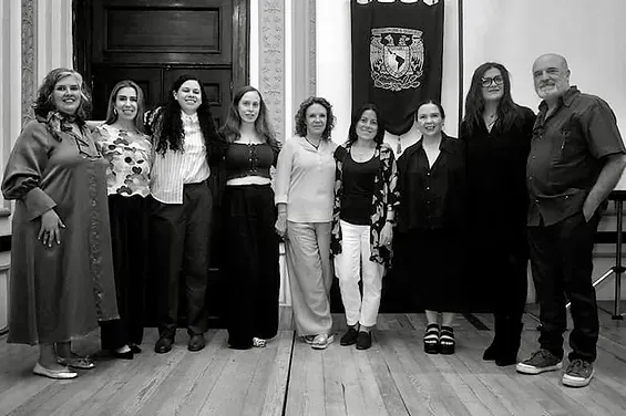 Grupo de personas posando para una foto en una habitación. Incluye una mujer y un hombre. Pancarta al fondo.