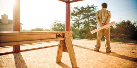 Un hombre está de pie sobre una plataforma de madera sosteniendo un plano.