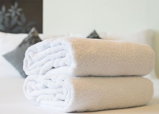 Dos toallas blancas están apiladas una encima de otra sobre una cama.