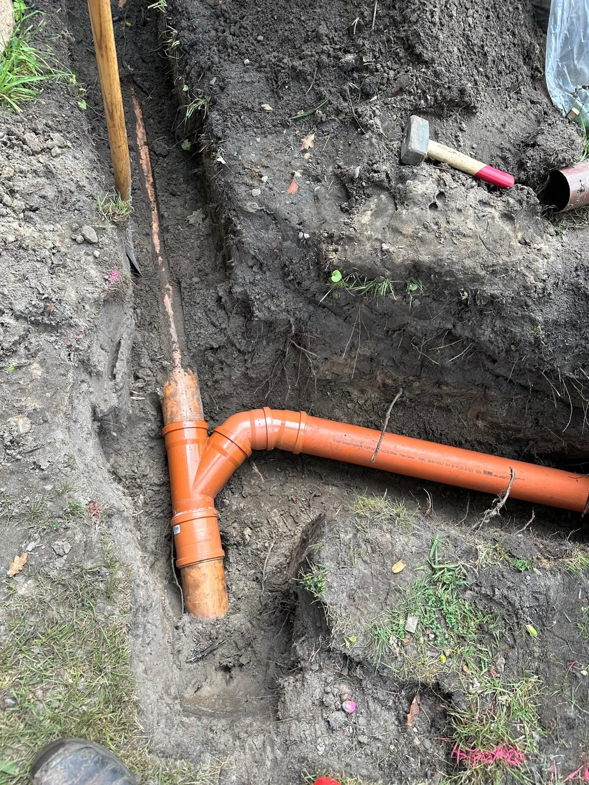 Eine Person gräbt ein Loch in den Boden, um ein Rohr zu verlegen.