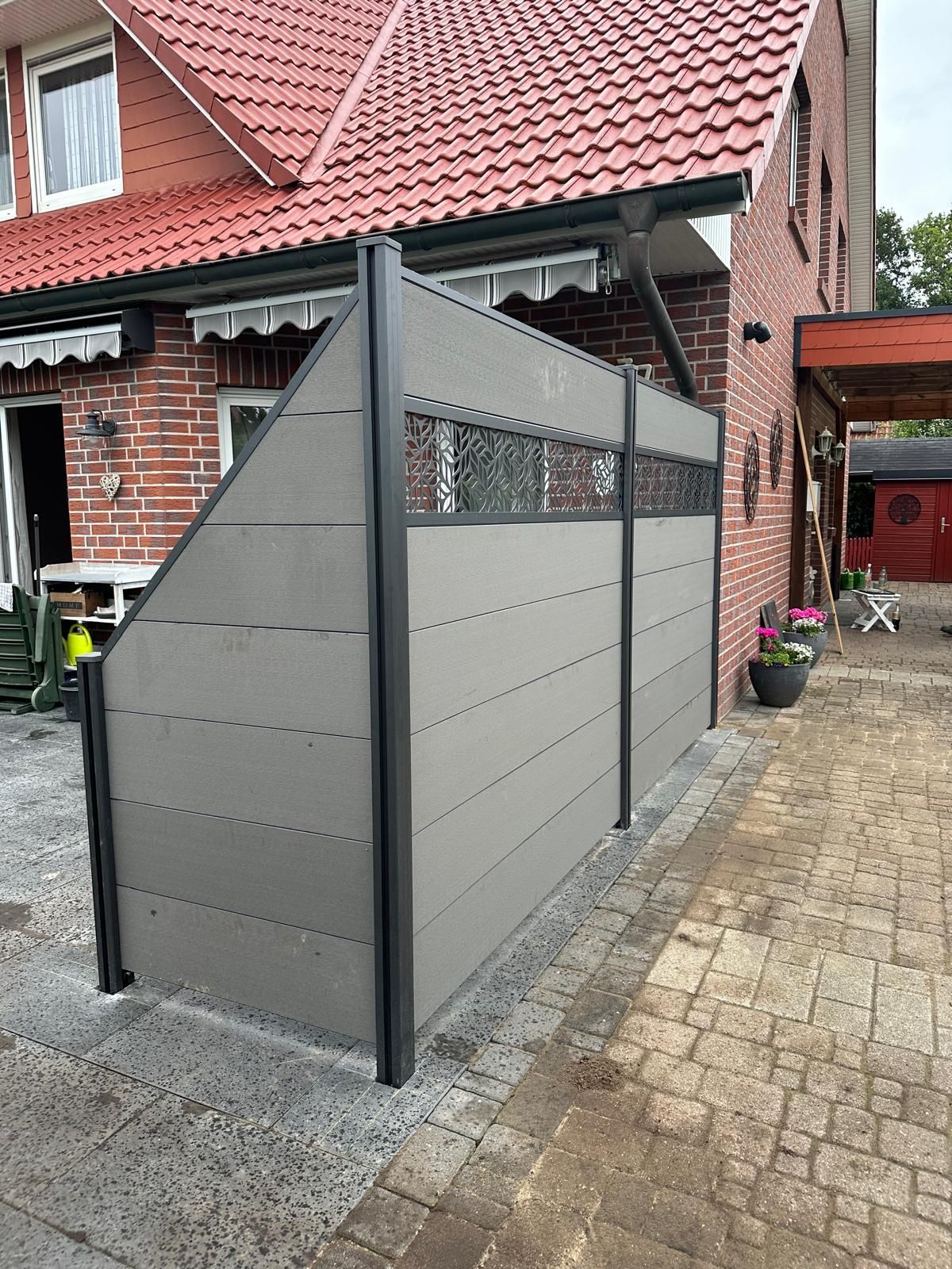 Vor einem Backsteinhaus steht ein Zaun.