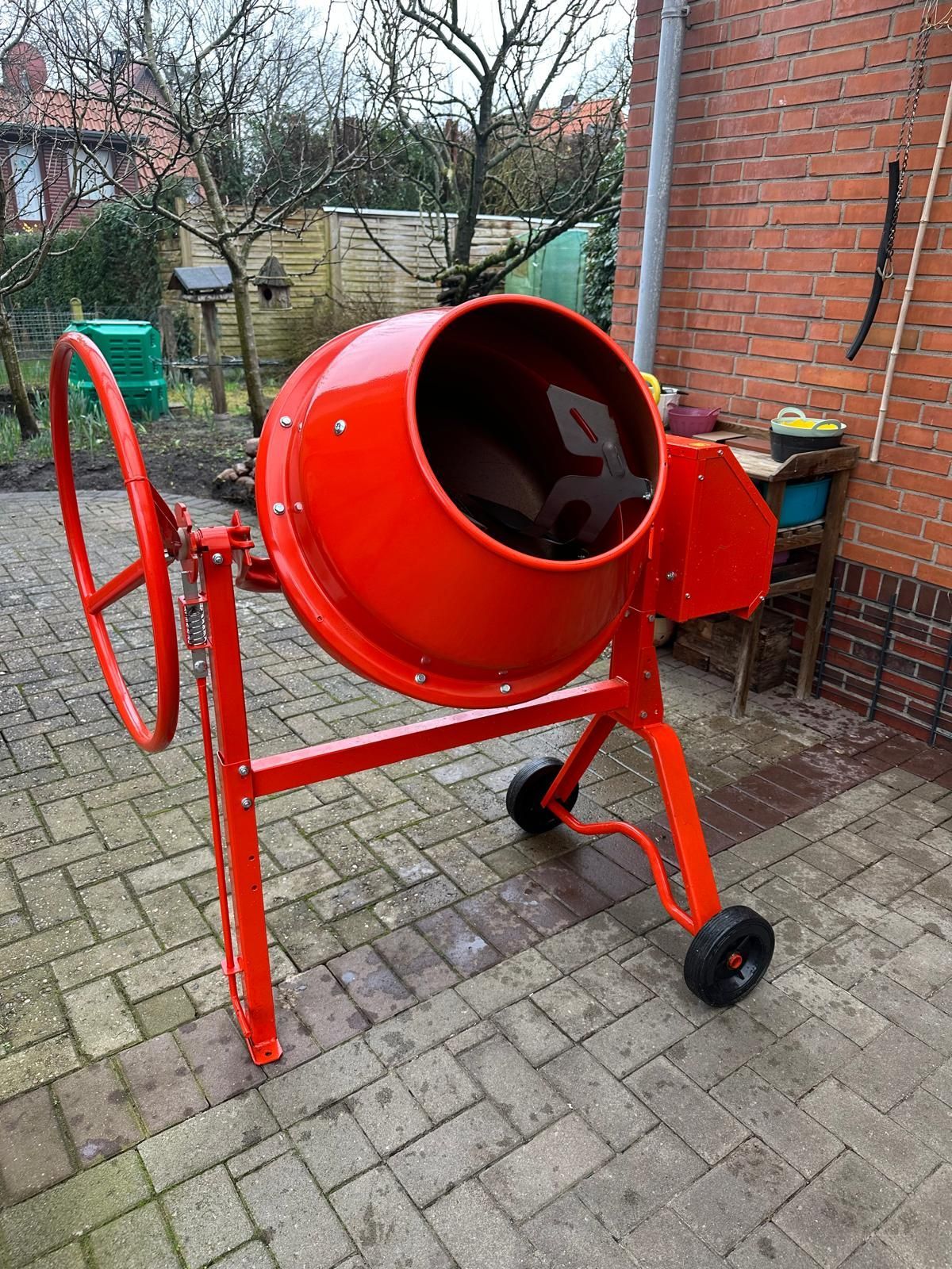 Ein roter Betonmischer steht auf einer gemauerten Terrasse vor einem Backsteingebäude.