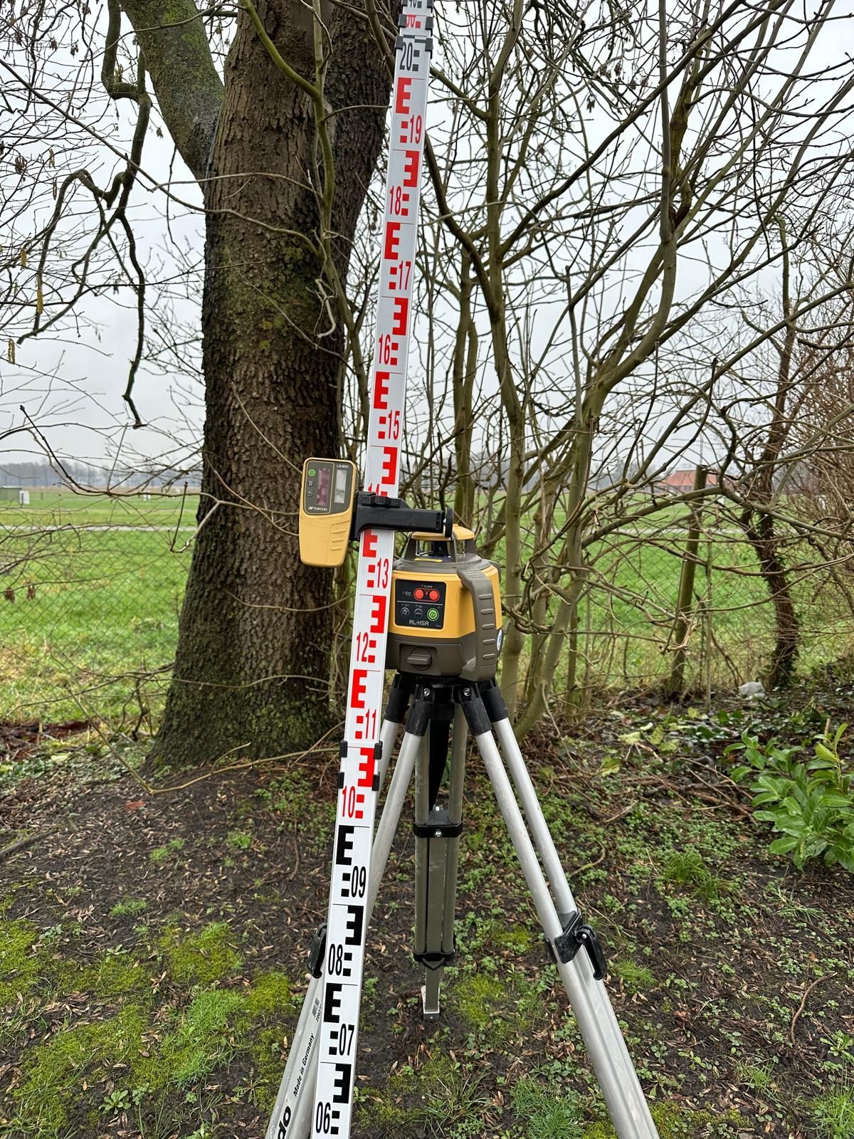 Eine Laserwasserwaage steht auf einem Stativ neben einem Baum.