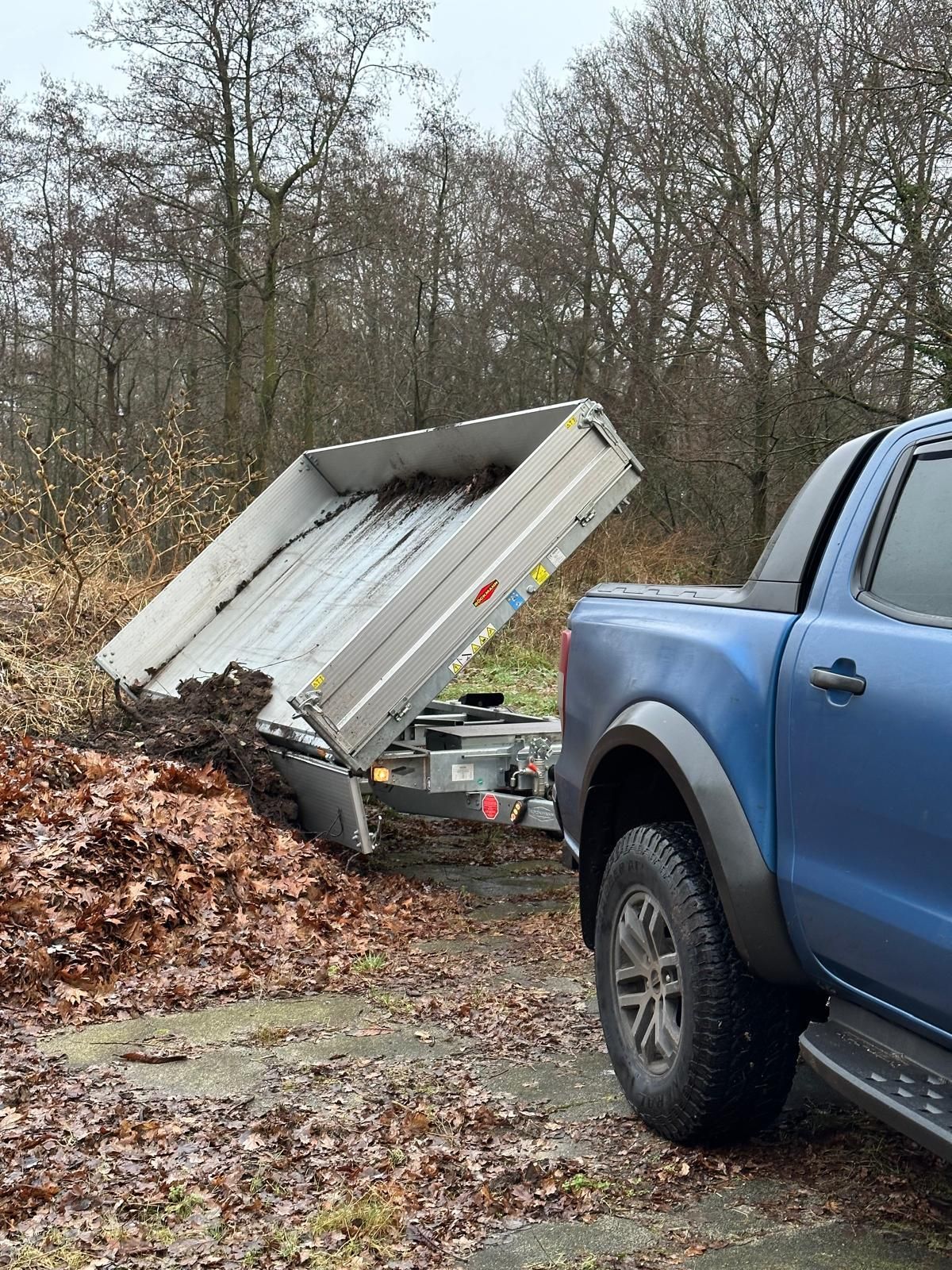 Ein blauer Lastwagen zieht einen mit Blättern gefüllten Kippanhänger.